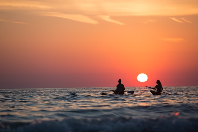 Couple sitting down on paddleboard watching the sunset